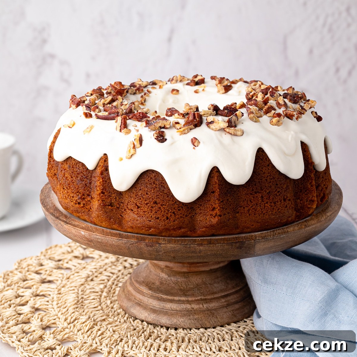 pumpkin cake frosted with cream cheese frosting and topped with chopped pecans on a wooden cake stand