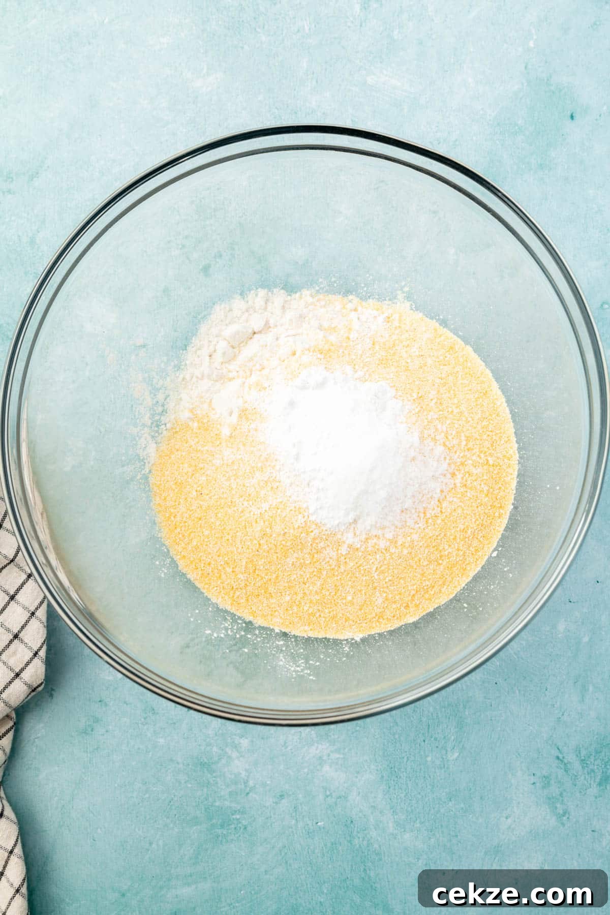 A glass mixing bowl with cornmeal, gluten-free flour, salt, baking soda, and baking powder before mixing.