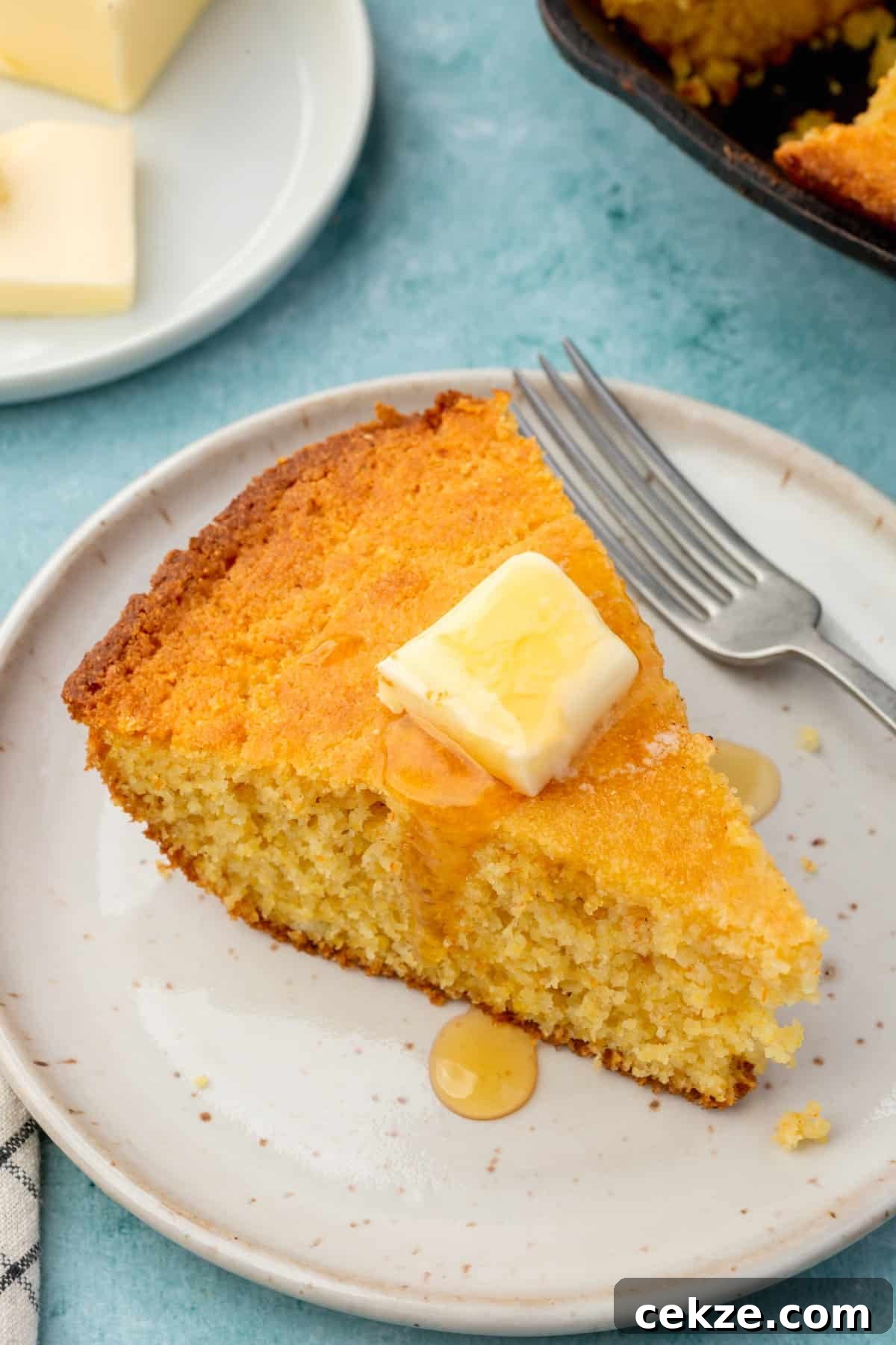 A wedge of gluten-free cornbread topped with melted butter and honey on an appetizer plate with a fork.